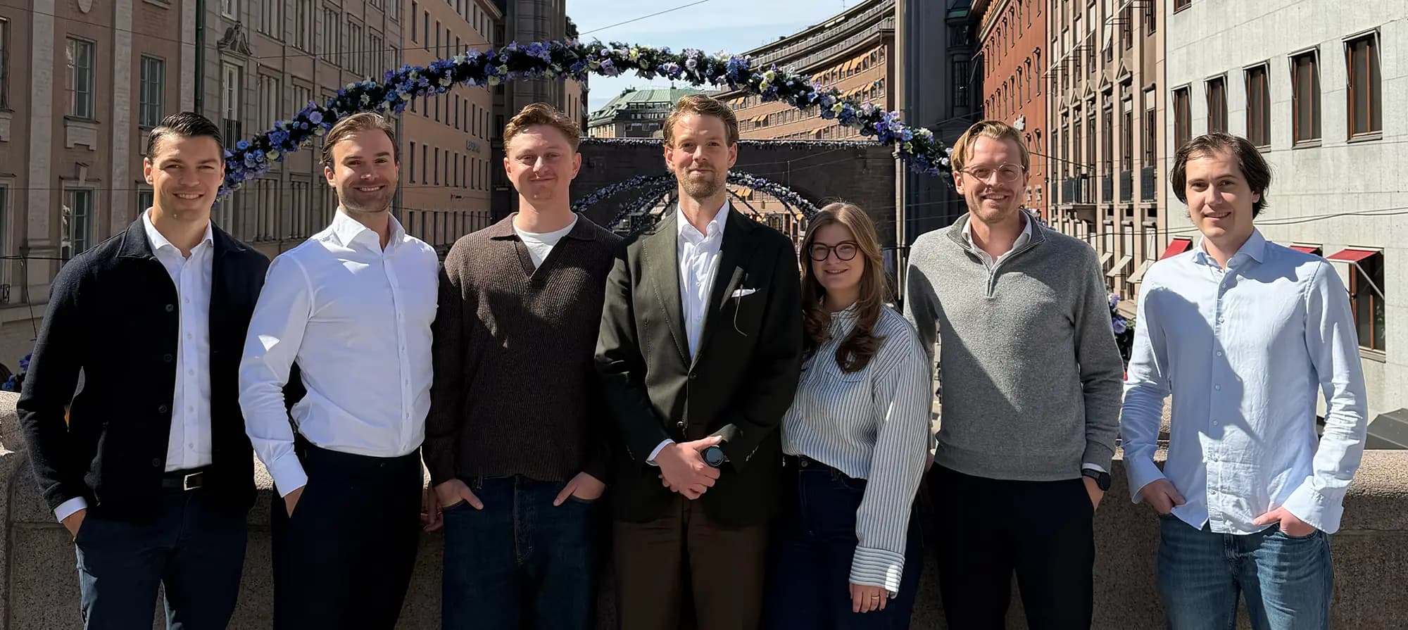 Sju personer från Selmas team står utomhus i Stockholm, framför en båge av blå och vita blommor.